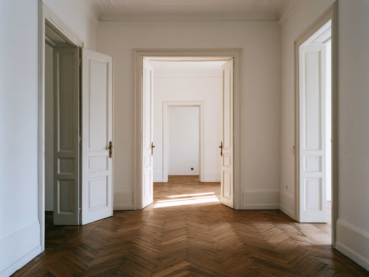 Interno dell'appartamento ristrutturato: infilata di porte allineate sul corridoio, parquet a spina di pesce e luce che arriva fino in fondo